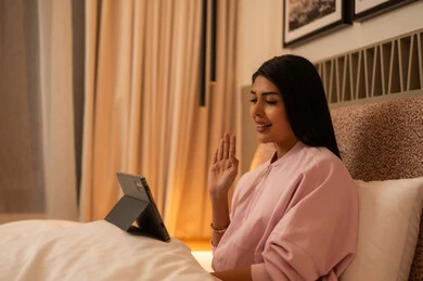 امرأة عربية في السرير تستخدم جهازاً لوحياً لمكالمة فيديو