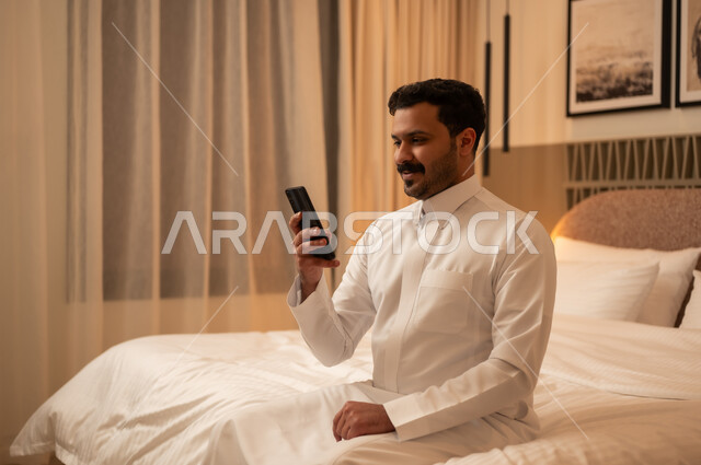رجل سعودي يستخدم الهاتف الذكي في غرفة نوم عصرية ليلاً