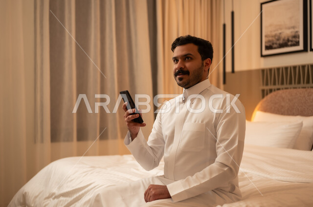 رجل سعودي بالثوب يستخدم الهاتف في غرفة النوم