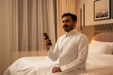 رجل سعودي بالثوب يستخدم الهاتف في غرفة النوم