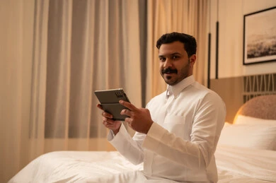 رجل سعودي مع جهاز لوحي في غرفة فندق