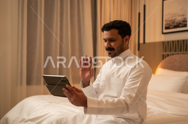 رجل سعودي يستخدم الجهاز اللوحي لمكالمة فيديو في غرفة النوم