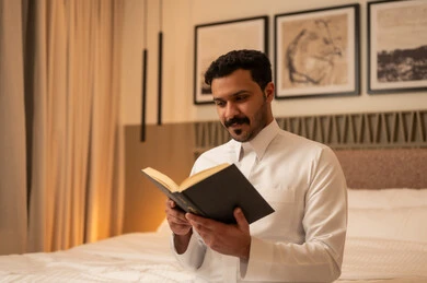 رجل سعودي بالثوب الأبيض يقرأ كتاباً في غرفة النوم