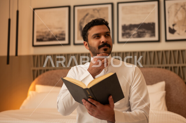 رجل سعودي يقرأ كتاباً بوضعية تفكير في غرفة نوم