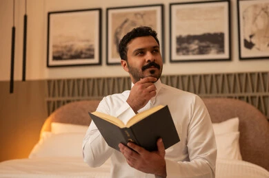 رجل سعودي يقرأ كتاباً بوضعية تفكير في غرفة نوم