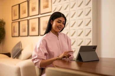 امرأة عربية تستخدم جهازاً لوحياً في غرفة معيشة حديثة