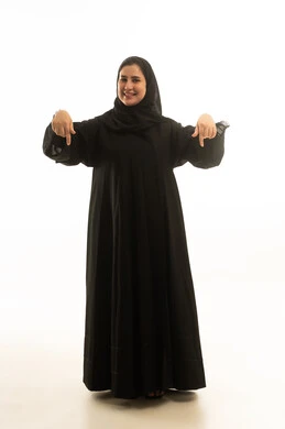 امرأة سعودية بالعباءة السوداء تشير للأسفل بخلفية بيضاء