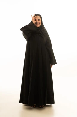 امرأة سعودية بالعباءة مبتسمة أمام خلفية بيضاء