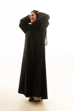 امرأة سعودية مبتسمة بالعباءة السوداء بخلفية بيضاء