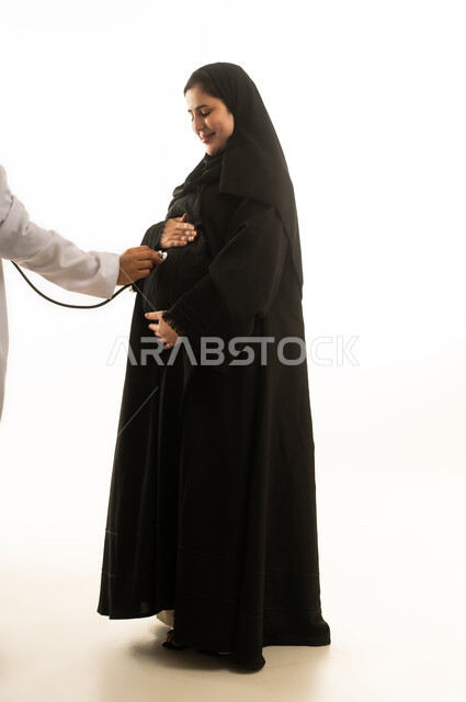 فحص طبي لامرأة سعودية حامل ترتدي عباءة بخلفية بيضاء