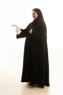 امرأة سعودية حامل تمسك ملابس مولود بخلفية بيضاء