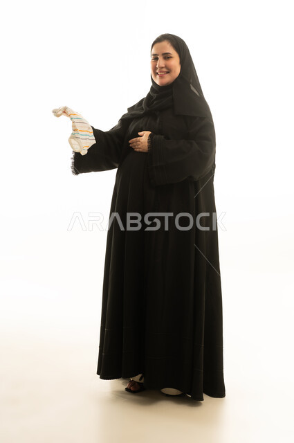 امرأة سعودية حامل تحمل جورب مولود بخلفية بيضاء