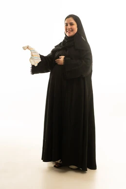 امرأة سعودية حامل تحمل جورب مولود بخلفية بيضاء