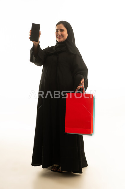 امرأة سعودية تحمل حقائب تسوق وهاتف ذكي