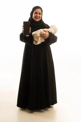 امرأة سعودية بالعباءة تحمل طفلاً وهاتف ذكي