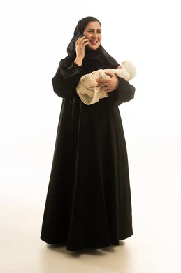 امرأة سعودية تحمل طفل رضيع وتستخدم الهاتف الذكي