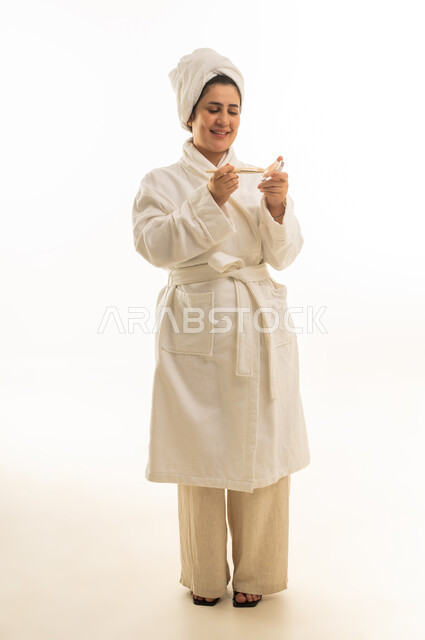 امرأة سعودية بروب استحمام أبيض تحمل أداة عناية بالبشرة