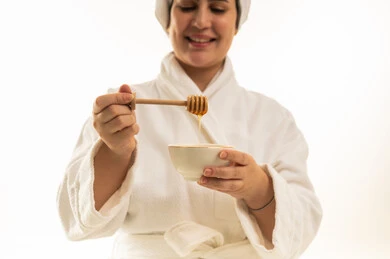 امرأة عربية برداء الحمام تستخدم العسل للعناية بالبشرة