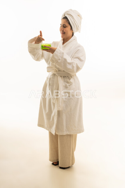 امرأة عربية برداء حمام تمسك بمنتج عناية بالبشرة