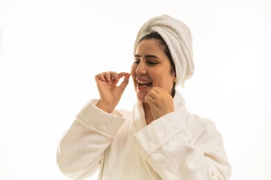 امرأة عربية ترتدي رداء حمام تستخدم خيط الأسنان