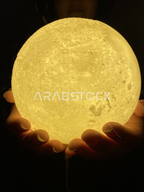 صورة مقرية ليد مرأة تحمل بيدها مصباح مضيء على شكل قمر ، ضوء القمر ، مفهوم الأمل ، القمر المتوهج ، مصباح القمر ، زينة رمضان ، شهر الخير ، رمضان كريم