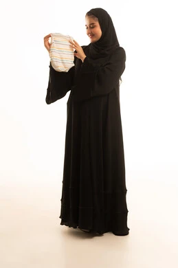 امرأة سعودية بالعباءة تحمل ملابس رضع خلفية بيضاء