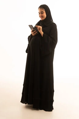 امرأة سعودية حامل تستخدم الجوال على خلفية بيضاء