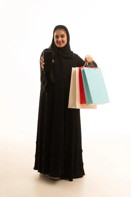 امرأة سعودية تحمل أكياس تسوق وهاتف ذكي