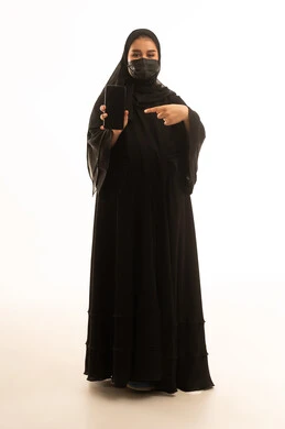 امرأة سعودية بالعباءة تشير إلى شاشة الهاتف الذكي