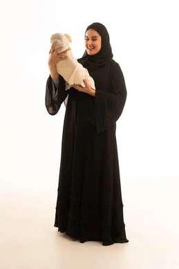 أم سعودية بالعباءة تحمل طفلها الرضيع خلفية بيضاء