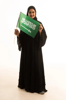 امرأة سعودية بالعباءة تحمل العلم السعودي خلفية بيضاء