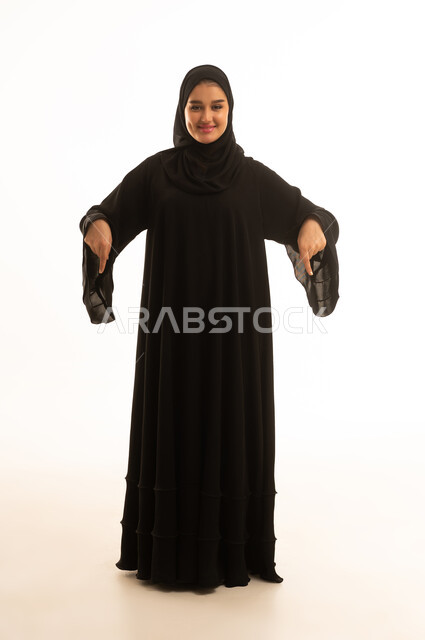 امرأة سعودية بالعباءة السوداء تشير للأسفل في استوديو