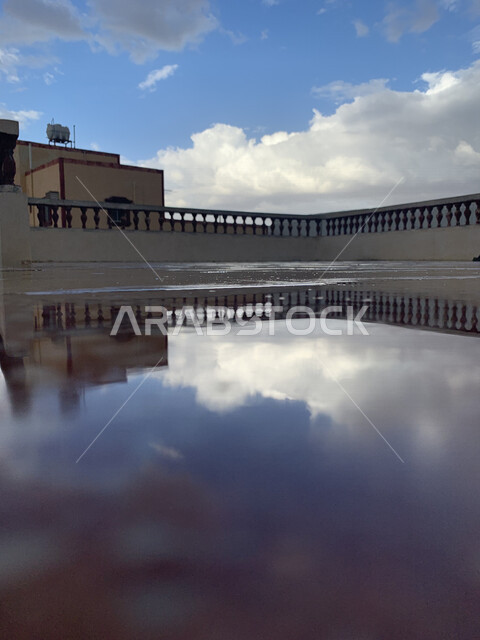 صورة إبادعية لإنعكاس السماء الزرقاء مع السحب البيضاء على بركة المياه بعد هطول الأمطار ، جمال الغيوم في سماء المملكة العربية السعودية  في مدينة الدمام 