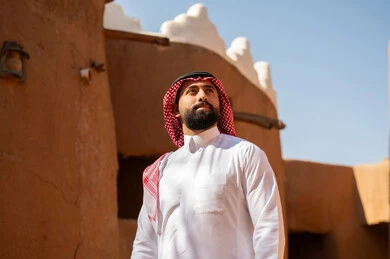 A Saudi Arabian Gulf Arab man wearing traditional attire, a white thobe and a shemagh, looks at something above. It is the anniversary of the establishment of the first Saudi state by Imam Muhammad bin Saud, which began on February 22, 1727. The historical and cultural depth of the Kingdom, national celebrations in the central region.