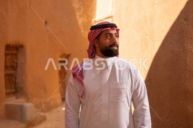 رجل عربي سعودي خليجي يرتدي الزي التقليدي ثوب أبيض وشماخ يقف بتعابير الثقة والجدية، ذكرى تأسيس الدوله السعوديه الاولى على يد الامام محمد بن سعود, يوم بدينا 22 فبراير 1727م, العمق التاريخي والحضاري للمملكة،الإحتفالات الوطنيه في المنطقه الوسطى