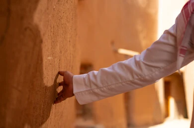 صورة من الجانب لرجل عربي سعودي خليجي يرتدي الزي التقليدي ثوب أبيض وشماخ يده على جدار طيني، ذكرى تأسيس الدوله السعوديه الاولى على يد الامام محمد بن سعود, يوم بدينا 22 فبراير 1727م, العمق التاريخي والحضاري للمملكة،الإحتفالات الوطنيه في المنطقه الوسطى