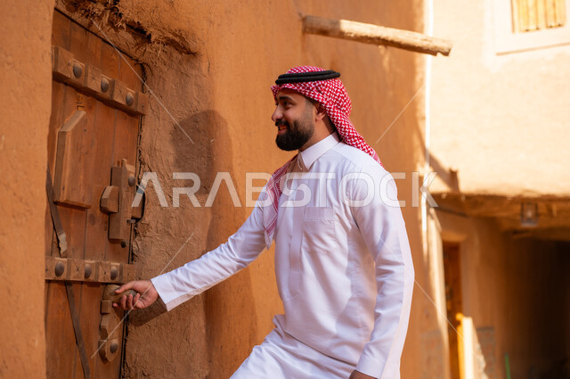 رجل عربي سعودي خليجي يرتدي الزي التقليدي ثوب أبيض وشماخ ويمسك باب خشبي، ذكرى تأسيس الدوله السعوديه الاولى على يد الامام محمد بن سعود, يوم بدينا 22 فبراير 1727م, العمق التاريخي والحضاري للمملكة،الإحتفالات الوطنيه في المنطقه الوسطى