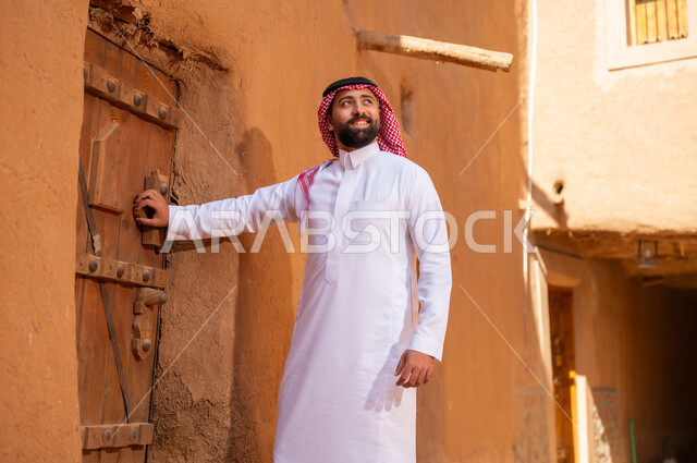 رجل عربي سعودي خليجي يرتدي زيالتقليدي ثوب أبيض ويمسك باب خشبي، ذكرى تأسيس الدوله السعوديه الاولى على يد الامام محمد بن سعود, يوم بدينا 22 فبراير 1727م, العمق التاريخي والحضاري للمملكة،الإحتفالات الوطنيه في المنطقه الوسطى