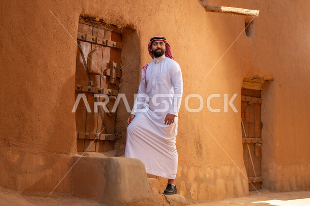 رجل عربي سعودي خليجي يرتدي زيالتقليدي ثوب أبيض ويمسك باب خشبي، ذكرى تأسيس الدوله السعوديه الاولى على يد الامام محمد بن سعود, يوم بدينا 22 فبراير 1727م, العمق التاريخي والحضاري للمملكة،الإحتفالات الوطنيه في المنطقه الوسطى