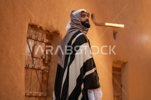 صورة من الخلف رجل عربي سعودي خليجي يرتدي زي يوم التأسيسي يقف أمام مبنى طيني وينظر الى شي ما في الأعلى، ذكرى تأسيس الدوله السعوديه الاولى على يد الامام محمد بن سعود, يوم بدينا 22 فبراير 1727م, العمق التاريخي والحضاري للمملكة،الإحتفالات الوطنيه في المنطقه الوسطى