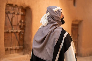 A picture from the back of an Arab Saudi Gulf man wearing the Foundation Day attire standing next to a mud building, commemorating the establishment of the first Saudi state by Imam Muhammad bin Saud, the day we began on February 22, 1727, the historical and cultural depth of the Kingdom, the identity of Saudi National Day 92. A picture from the back of an Arab Saudi Gulf man wearing the Foundation Day attire standing next to a mud building, commemorating the establishment of the first Saudi state by Imam Muhammad bin Saud, the day we began on February 22, 1727, the historical and cultural depth of the Kingdom, the identity of Saudi National Day 92.