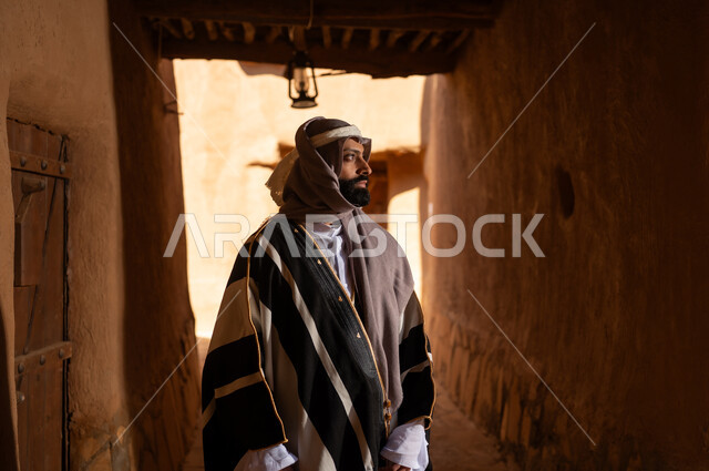 صورة من الجانب رجل عربي سعودي خليجي يرتدي زي يوم التأسيسي يقف داخل مبنى طيني, ذكرى تأسيس الدوله السعوديه الاولى على يد الامام محمد بن سعود, يوم بدينا 22 فبراير 1727م, العمق التاريخي والحضاري للمملكة، هوية اليوم الوطني السعودي 92