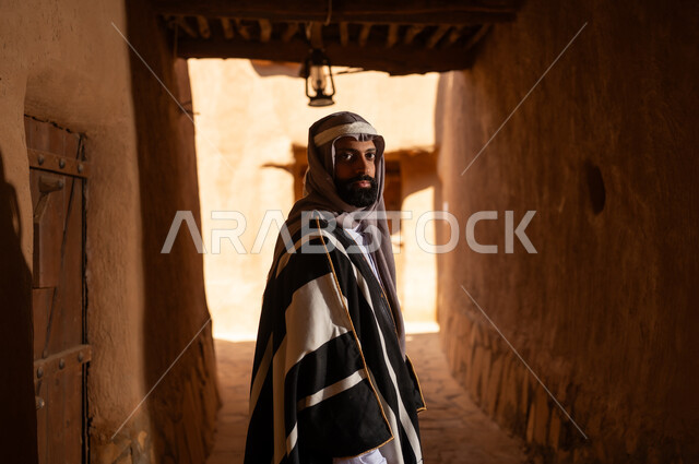 صورة من الجانب رجل عربي سعودي خليجي يرتدي زي يوم التأسيسي يقف داخل مبنى طيني, ذكرى تأسيس الدوله السعوديه الاولى على يد الامام محمد بن سعود, يوم بدينا 22 فبراير 1727م, العمق التاريخي والحضاري للمملكة، هوية اليوم الوطني السعودي 92