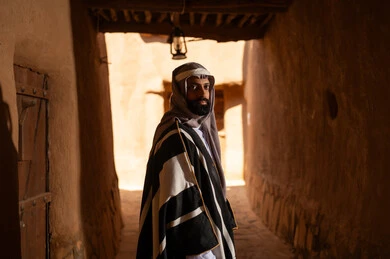 صورة من الجانب رجل عربي سعودي خليجي يرتدي زي يوم التأسيسي يقف داخل مبنى طيني, ذكرى تأسيس الدوله السعوديه الاولى على يد الامام محمد بن سعود, يوم بدينا 22 فبراير 1727م, العمق التاريخي والحضاري للمملكة، هوية اليوم الوطني السعودي 92