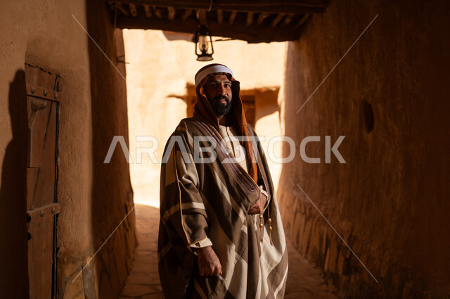 رجل عربي سعودي خليجي يرتدي زي يوم التأسيسي يقف داخل مبنى طيني, ذكرى تأسيس الدوله السعوديه الاولى على يد الامام محمد بن سعود, يوم بدينا 22 فبراير 1727م, العمق التاريخي والحضاري للمملكة، هوية اليوم الوطني السعودي 92