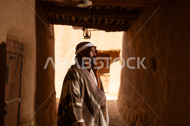 صورة من الجانب رجل عربي سعودي خليجي يرتدي زي يوم التأسيسي يقف داخل مبنى طيني, ذكرى تأسيس الدوله السعوديه الاولى على يد الامام محمد بن سعود, يوم بدينا 22 فبراير 1727م, العمق التاريخي والحضاري للمملكة، هوية اليوم الوطني السعودي 92