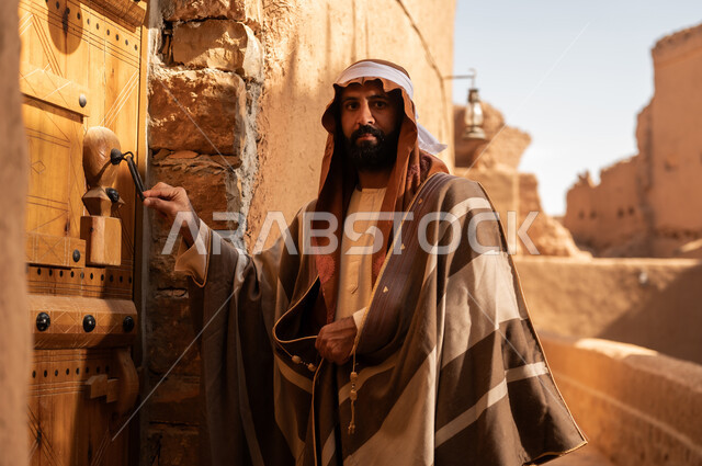 رجل عربي سعودي خليجي يرتدي زي يوم التأسيس يطرق باب خشبي لمبنى طيني, ذكرى تأسيس الدوله السعوديه الاولى على يد الامام محمد بن سعود, يوم بدينا 22 فبراير 1727م, العمق التاريخي والحضاري للمملكة، هوية اليوم الوطني السعودي 92