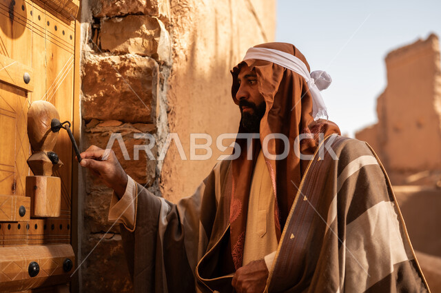 رجل عربي سعودي خليجي يرتدي زي يوم التأسيس يطرق باب خشبي لمبنى طيني, ذكرى تأسيس الدوله السعوديه الاولى على يد الامام محمد بن سعود, يوم بدينا 22 فبراير 1727م, العمق التاريخي والحضاري للمملكة، هوية اليوم الوطني السعودي 92