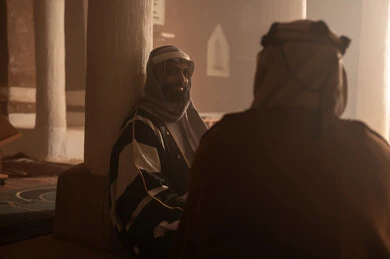 An elderly Arab Saudi Gulf man wearing a bisht and agal on Foundation Day is sitting with a man inside a mud building, commemorating the establishment of the first Saudi state by Imam Muhammad bin Saud, on the day we began, February 22, 1727. The historical and cultural depth of the Kingdom, wearing traditional attire reflects the heritage.