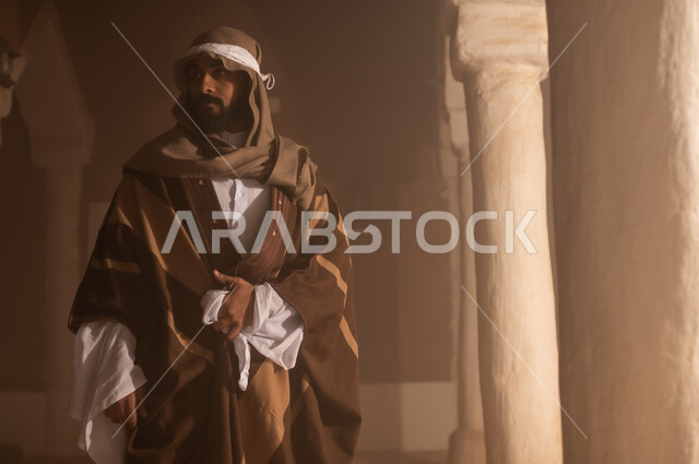 رجل كبير السن عربي سعودي خليجي يرتدي البشت وعقال يوم التأسيس يقف  داخل مبنى طيني تفاصيل العمارة القديمة, ذكرى تأسيس الدوله السعوديه الاولى على يد الامام محمد بن سعود, يوم بدينا 22 فبراير 1727م, العمق التاريخي والحضاري للمملكة، ارتداء الأزياء التقليدية تعكس التراث